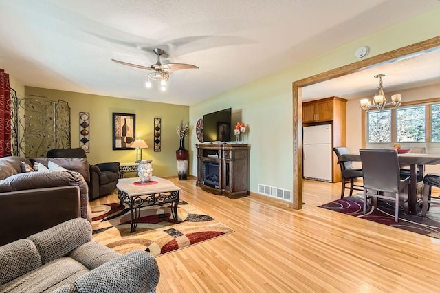 living room featuring ceiling fan with notable chandelier and light hardwood / wood-style flooring