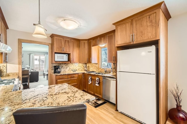 kitchen with sink, white appliances, tasteful backsplash, light stone countertops, and decorative light fixtures