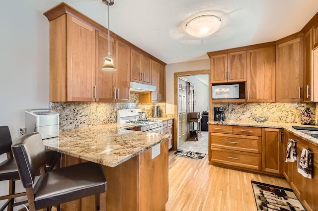 kitchen featuring decorative light fixtures, a kitchen bar, light hardwood / wood-style floors, light stone counters, and white appliances