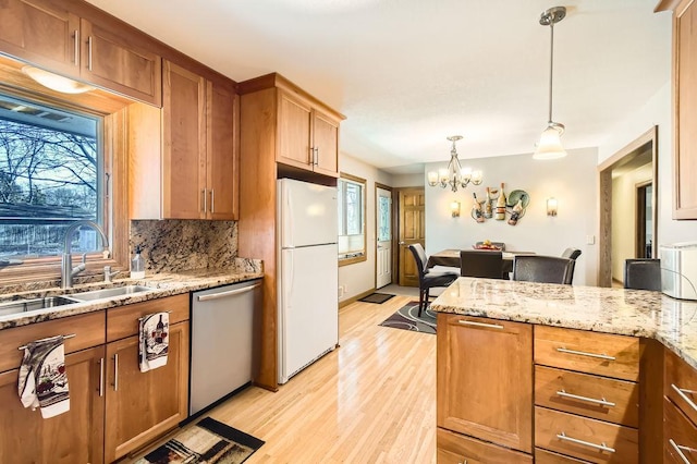 kitchen with pendant lighting, sink, white fridge, stainless steel dishwasher, and light stone counters