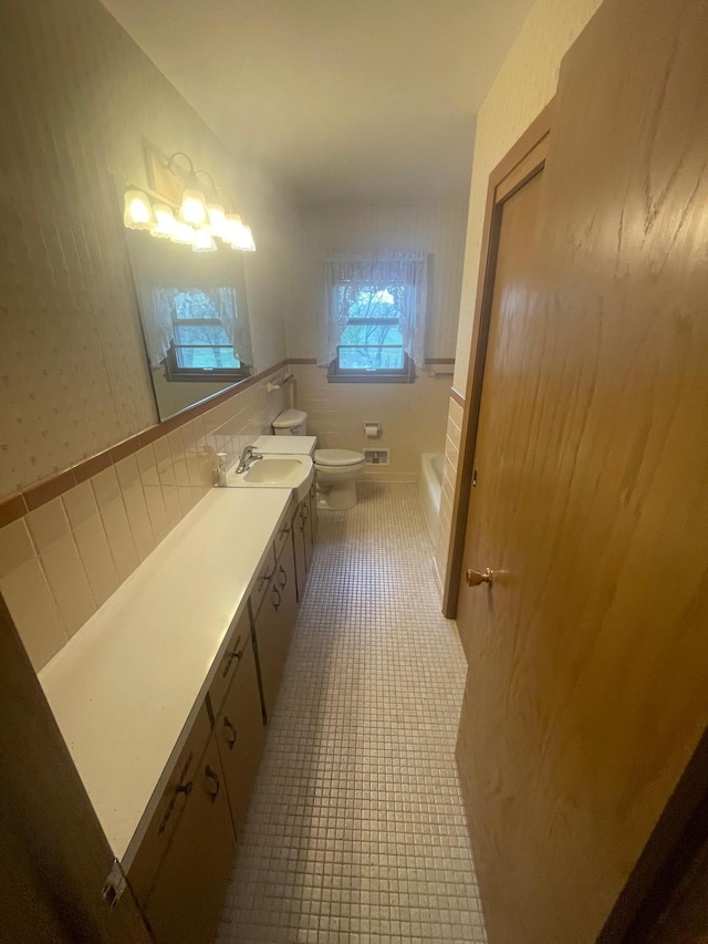 bathroom featuring tile patterned floors, a bathtub, vanity, tile walls, and toilet