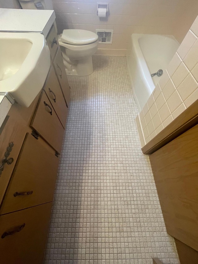 bathroom with vanity, tile patterned flooring, a washtub, toilet, and tile walls