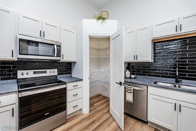 kitchen with appliances with stainless steel finishes, light hardwood / wood-style floors, white cabinetry, and sink