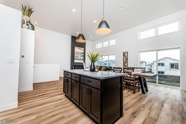 kitchen with a high ceiling, light hardwood / wood-style flooring, hanging light fixtures, and dark stone countertops