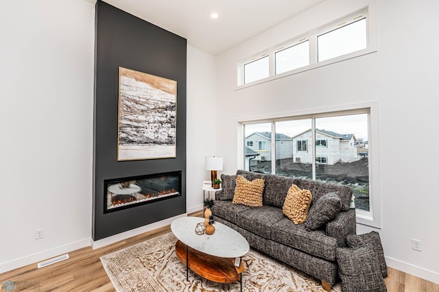 living room with a wealth of natural light, a fireplace, a high ceiling, and light hardwood / wood-style flooring