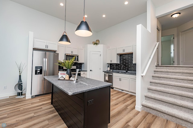 kitchen with light stone counters, appliances with stainless steel finishes, a kitchen island with sink, white cabinets, and light wood-type flooring