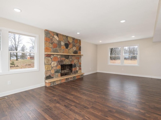 unfurnished living room with a stone fireplace, dark wood-type flooring, and a wealth of natural light