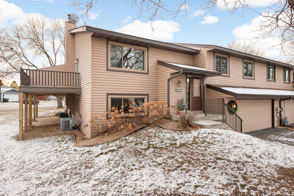 raised ranch featuring a balcony, a garage, and central air condition unit