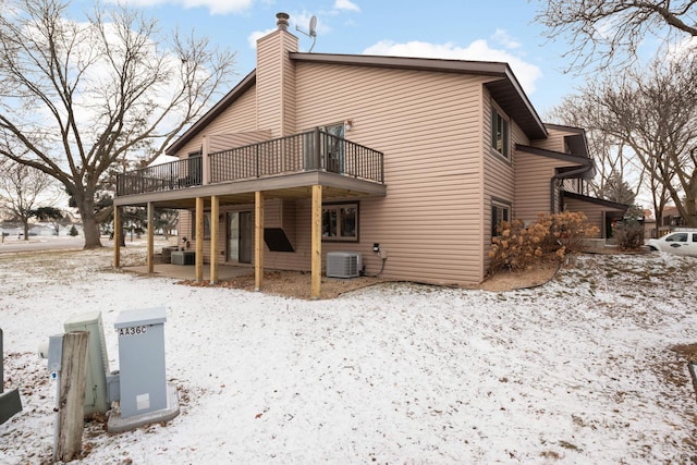 snow covered back of property with central AC unit and a wooden deck