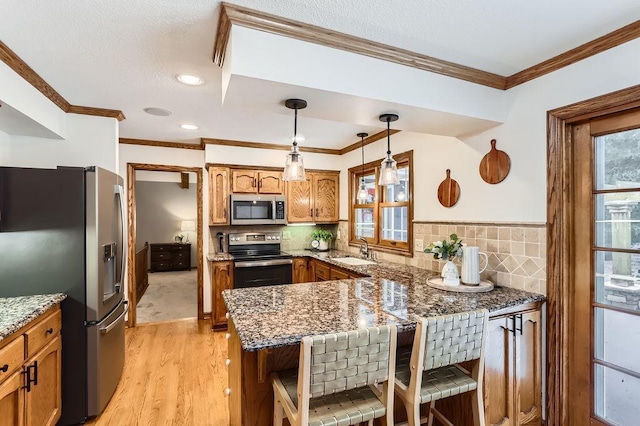 kitchen featuring pendant lighting, appliances with stainless steel finishes, dark stone countertops, a kitchen bar, and kitchen peninsula