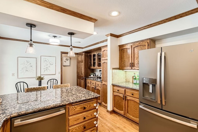 kitchen featuring crown molding, decorative light fixtures, appliances with stainless steel finishes, dark stone counters, and backsplash