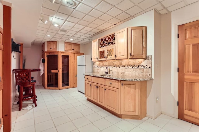 kitchen featuring sink, tasteful backsplash, light brown cabinets, white refrigerator, and light stone countertops