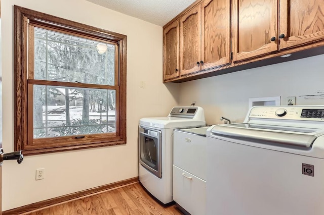 clothes washing area featuring plenty of natural light, washing machine and dryer, cabinets, and light wood-type flooring