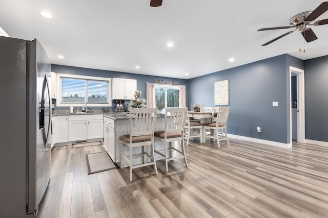 kitchen featuring white cabinetry, a center island, a kitchen bar, stainless steel fridge with ice dispenser, and light wood-type flooring