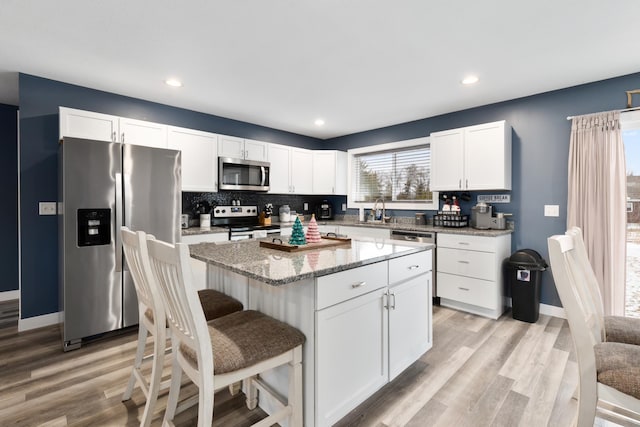 kitchen with sink, stainless steel appliances, light stone countertops, white cabinets, and a kitchen island