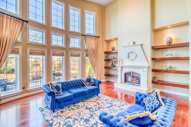 living room with hardwood / wood-style flooring, plenty of natural light, built in shelves, and a towering ceiling