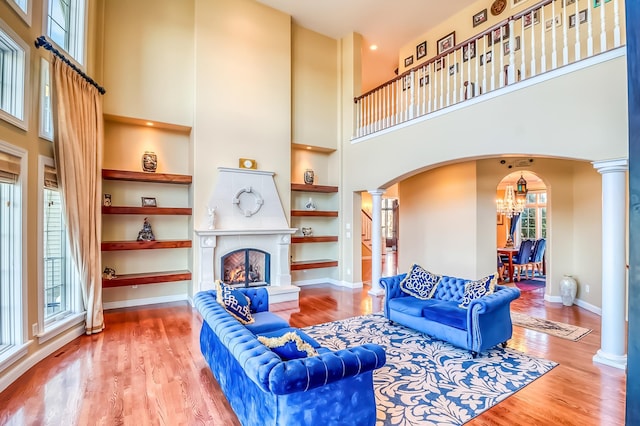 living room featuring decorative columns, hardwood / wood-style floors, a towering ceiling, and a notable chandelier