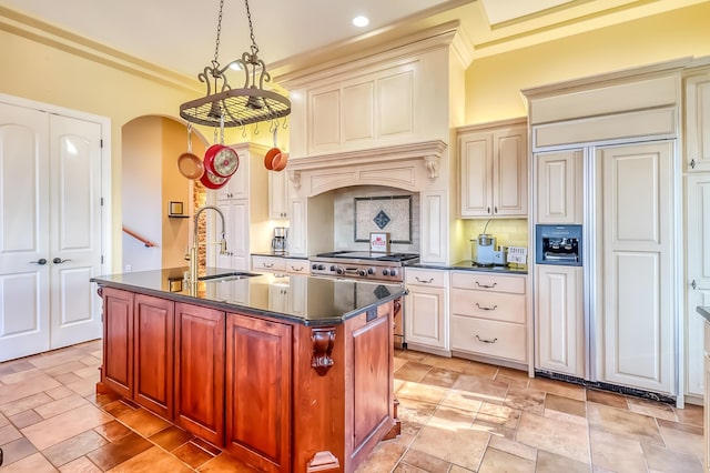 kitchen with a center island with sink, decorative backsplash, paneled built in fridge, cream cabinets, and sink