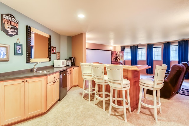 kitchen with dishwasher, light brown cabinets, light carpet, sink, and a breakfast bar