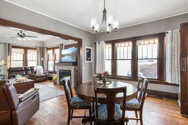 dining room featuring ceiling fan with notable chandelier, ornamental molding, a brick fireplace, a textured ceiling, and light hardwood / wood-style flooring