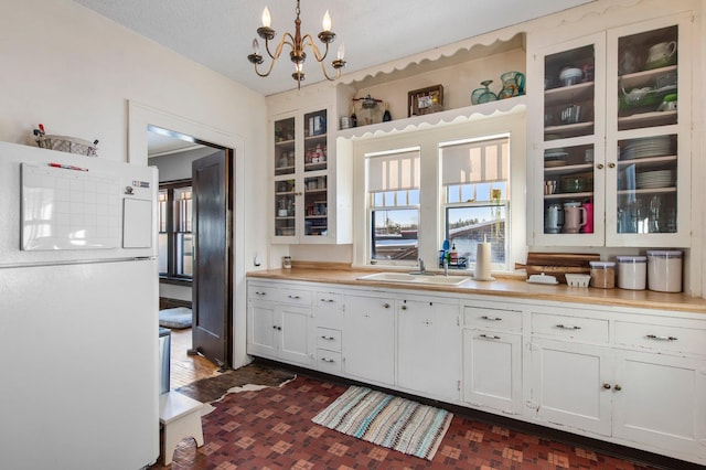 kitchen with a wealth of natural light, pendant lighting, sink, white cabinets, and white refrigerator