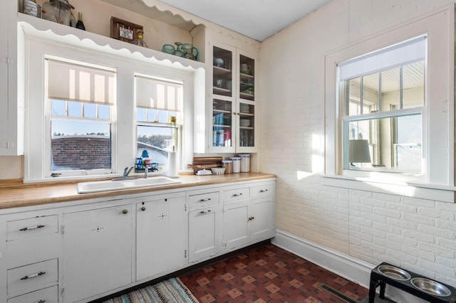 kitchen with brick wall, sink, white cabinets, and plenty of natural light