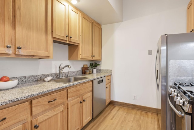 kitchen with light brown cabinetry, sink, light stone counters, stainless steel appliances, and light hardwood / wood-style flooring