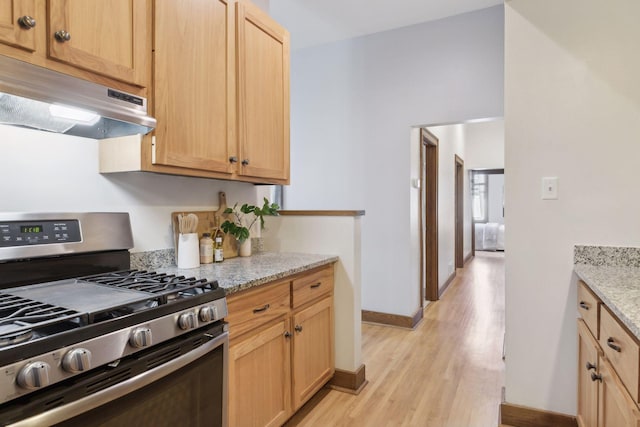 kitchen with light stone counters, light brown cabinetry, stainless steel gas range oven, and light wood-type flooring