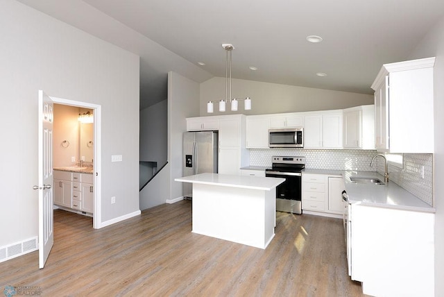 kitchen with appliances with stainless steel finishes, sink, pendant lighting, a center island, and light hardwood / wood-style floors