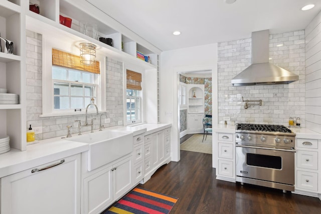 kitchen with wall chimney range hood, sink, dark hardwood / wood-style floors, premium stove, and white cabinets