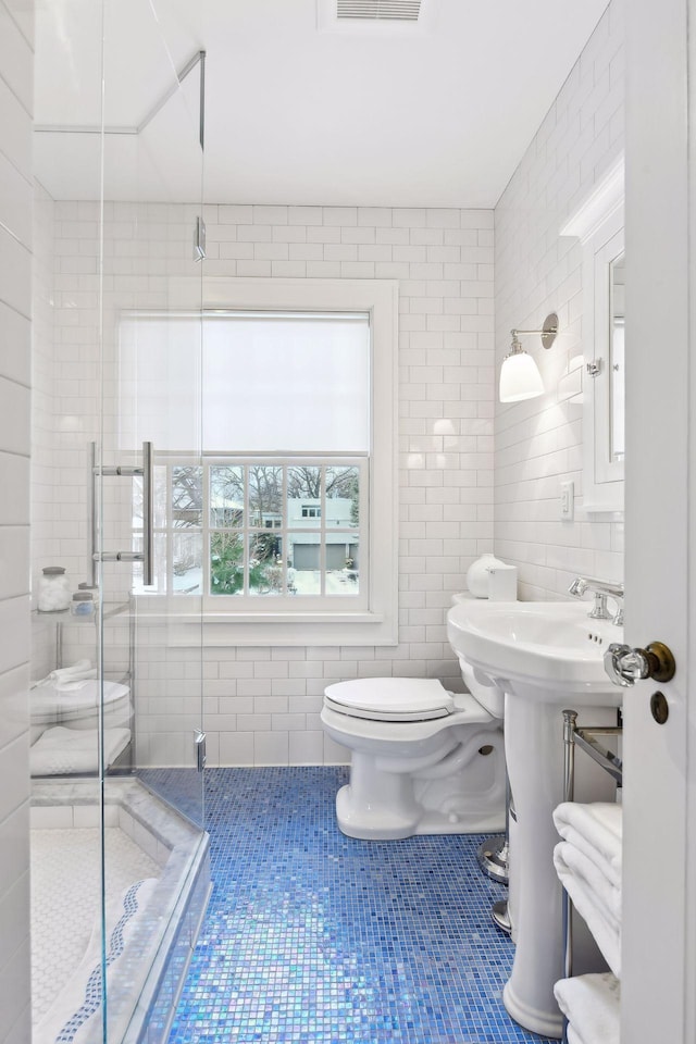 bathroom featuring tile patterned floors, toilet, an enclosed shower, sink, and tile walls