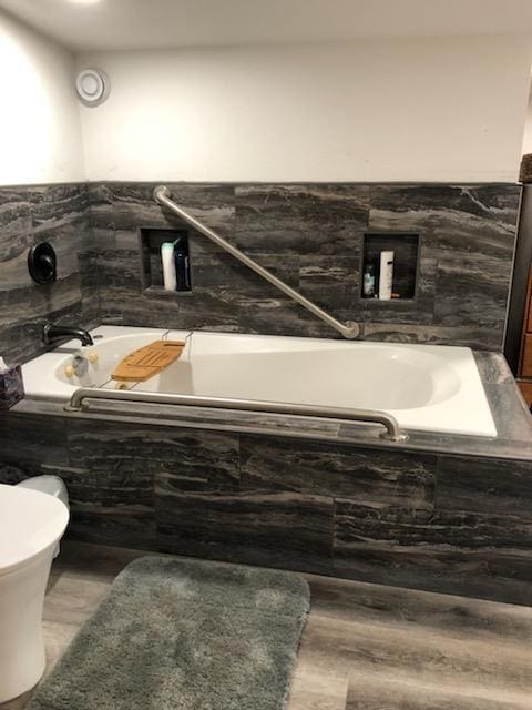 bathroom featuring tiled tub, hardwood / wood-style floors, and toilet