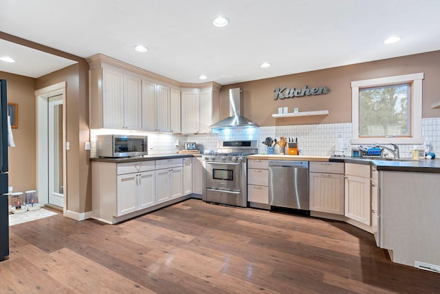 kitchen with hardwood / wood-style flooring, stainless steel appliances, a sink, wall chimney range hood, and decorative backsplash