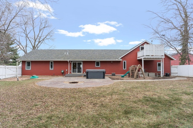 back of house with a hot tub, a patio area, a fenced backyard, and a lawn