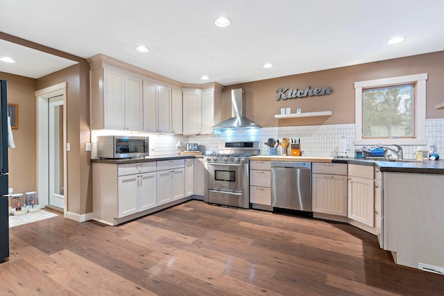 kitchen with a sink, wall chimney exhaust hood, wood-type flooring, stainless steel appliances, and decorative backsplash