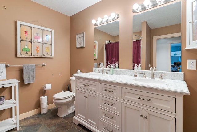 bathroom with baseboards, double vanity, a sink, and toilet