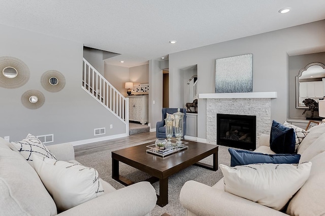 living room featuring a stone fireplace, a textured ceiling, and hardwood / wood-style flooring