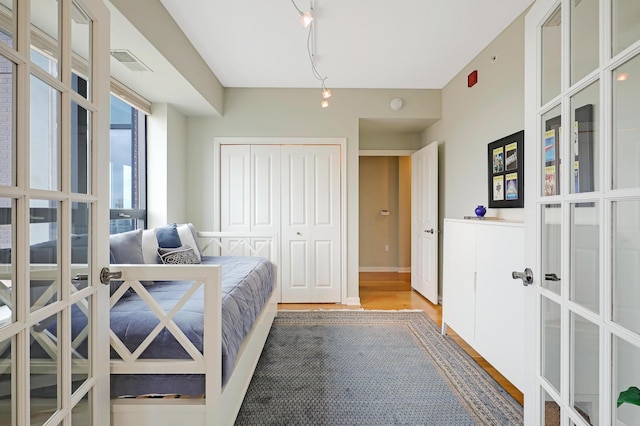 bedroom featuring a closet, rail lighting, french doors, and hardwood / wood-style flooring