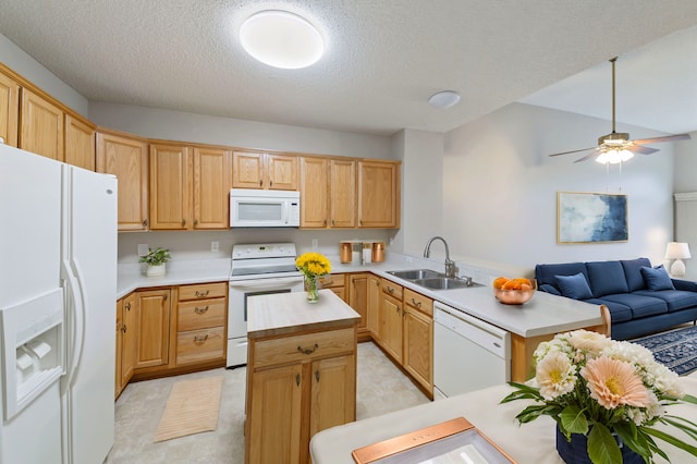 kitchen with a kitchen island, open floor plan, a peninsula, white appliances, and a sink