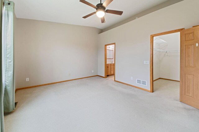 unfurnished bedroom featuring light carpet, ceiling fan, a spacious closet, connected bathroom, and a closet