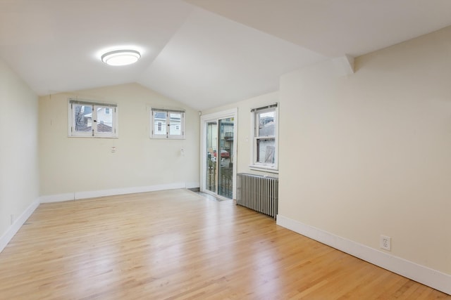 empty room featuring lofted ceiling, light wood-type flooring, and radiator heating unit