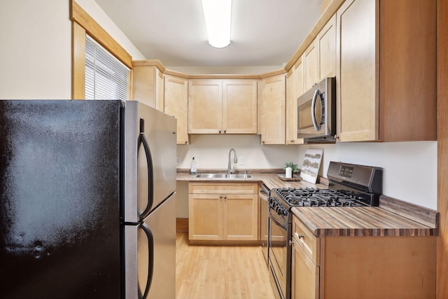 kitchen featuring light brown cabinetry, butcher block counters, sink, stainless steel appliances, and light hardwood / wood-style flooring