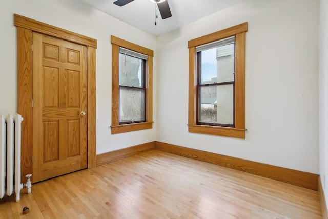 empty room with ceiling fan, radiator heating unit, light hardwood / wood-style floors, and plenty of natural light