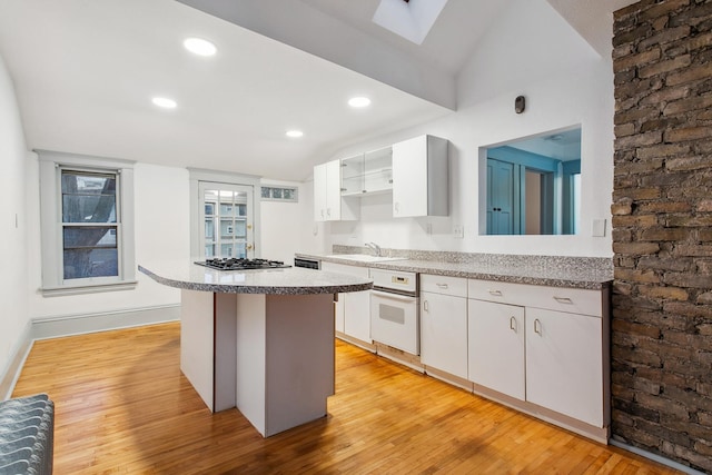 kitchen featuring sink, white cabinetry, light wood-type flooring, a kitchen island, and oven