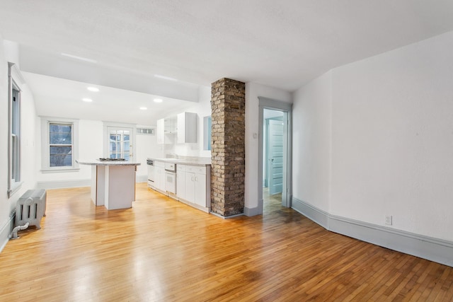 kitchen with radiator, light hardwood / wood-style flooring, white cabinets, a kitchen island, and oven