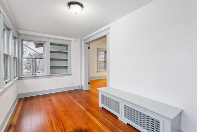 empty room featuring hardwood / wood-style floors, built in shelves, and radiator heating unit