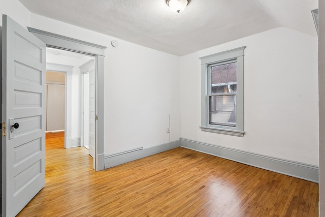 empty room featuring vaulted ceiling, a textured ceiling, and light hardwood / wood-style floors