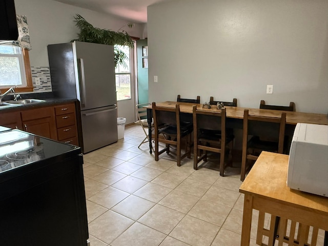 kitchen with stainless steel fridge, light tile patterned floors, black / electric stove, and sink