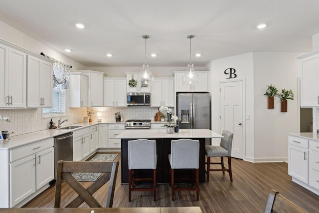 kitchen with appliances with stainless steel finishes, white cabinetry, hanging light fixtures, and a kitchen island