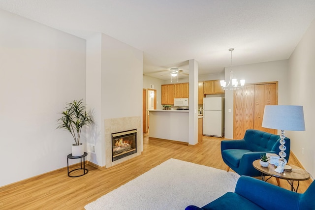 living room featuring ceiling fan with notable chandelier, a fireplace, and light hardwood / wood-style flooring